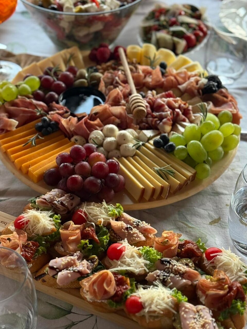 Drvena daska sa sirevima, pršutom, grožđem i kanapeima