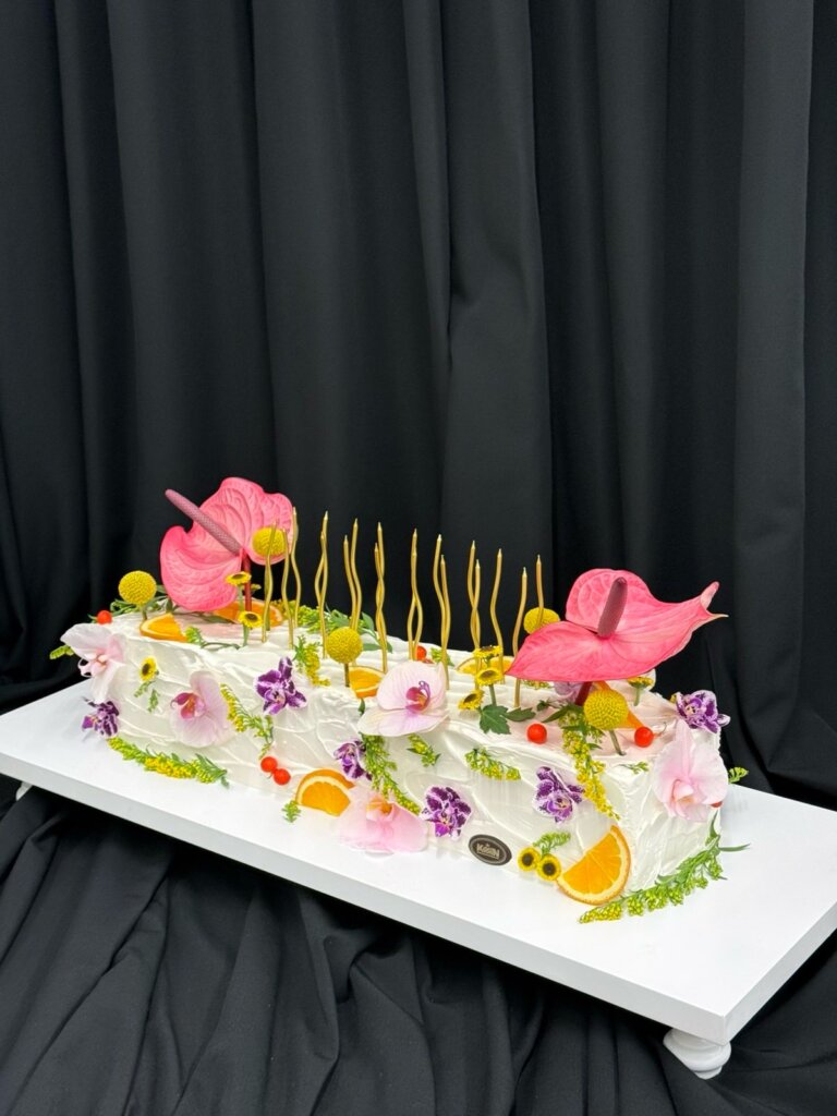 Dugačka bela torta sa roze anturijumima, orhidejama i zlatnim svećicama