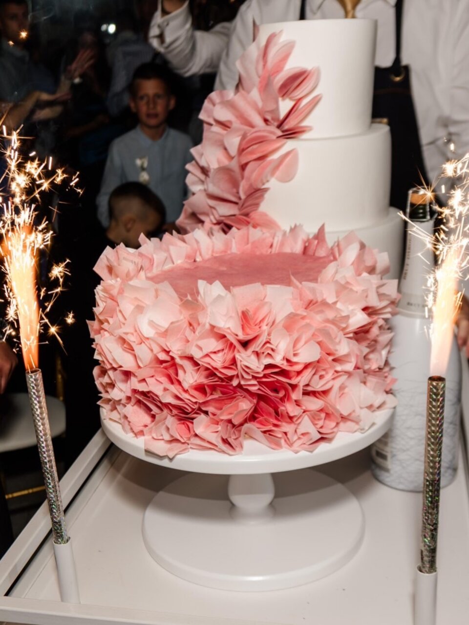 Trospratna bela torta sa roze ruffle cvetom i prskalicama