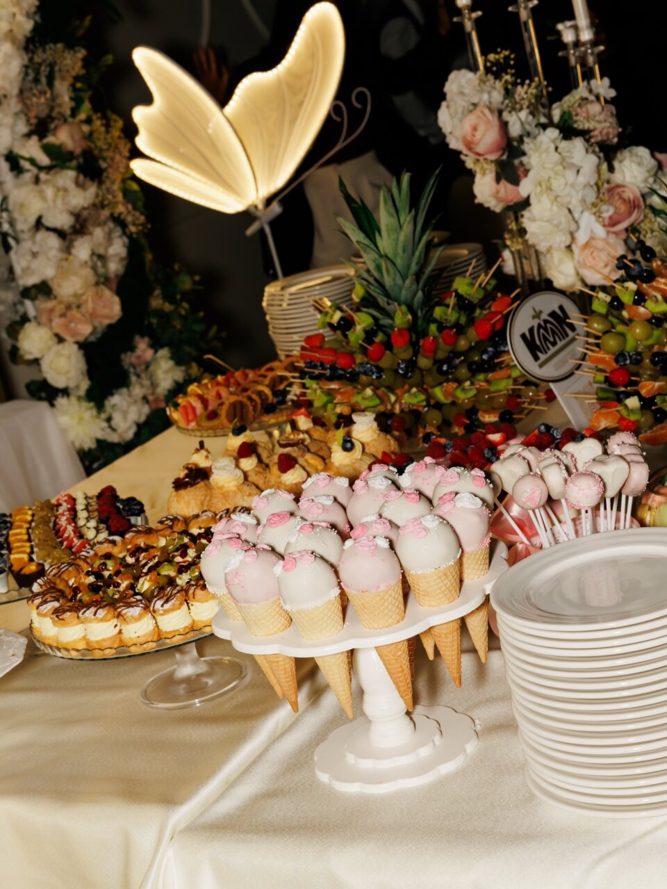 Svečani slatki sto sa svetlećim leptirom i cake pops kornetima