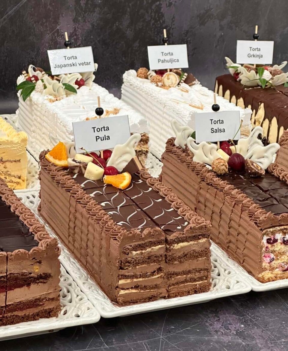Torte na kriške u poslastičarskoj vitrini sa nazivima ukusa