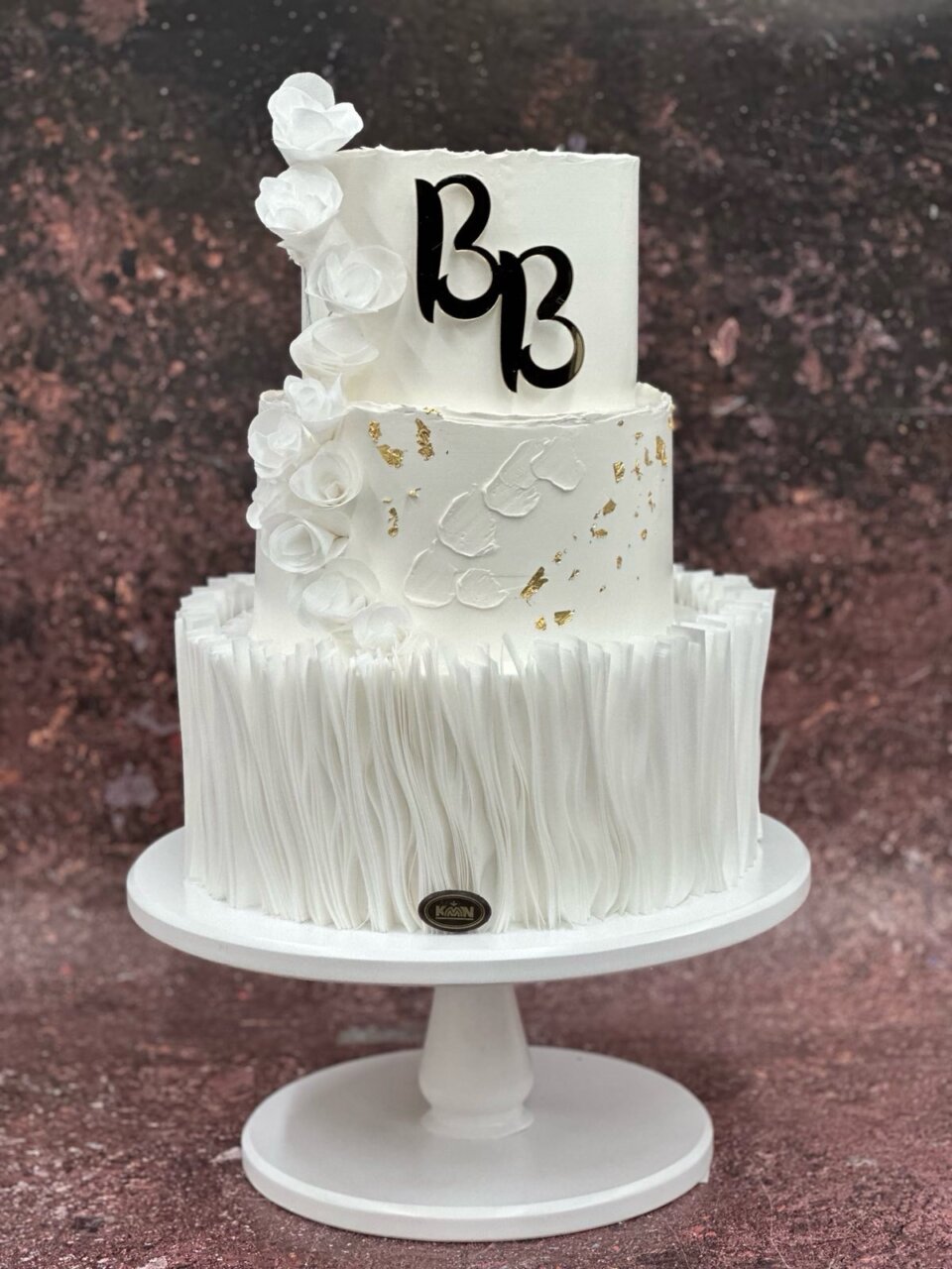 Trospratna bela svadbena torta sa ruffle teksturom i monogramom